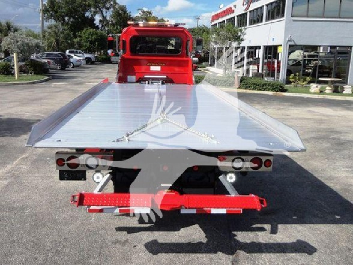 Peterbilt 337 rollback tow truck with a flatbed, rear view showing aluminum deck and red chassis, present at dealership lot.