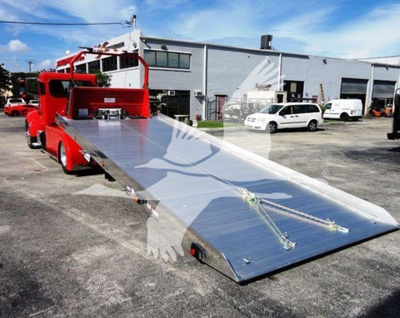 2022 Peterbilt 337 rollback truck with a lowered aluminum ramp bed, red chassis, and white building background.