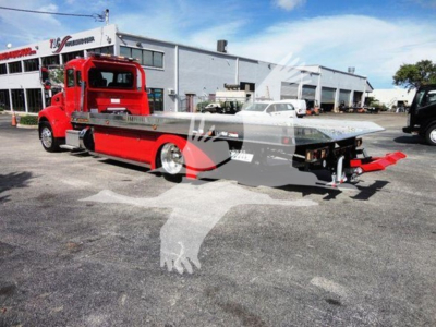 2022 Peterbilt 337 rollback truck in red and gray with flatbed, side view, dealership lot in background.