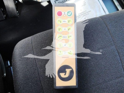 Upholstered truck seat with a beige remote control featuring circular yellow buttons and a round logo at the bottom, inside a Peterbilt rollback truck cabin