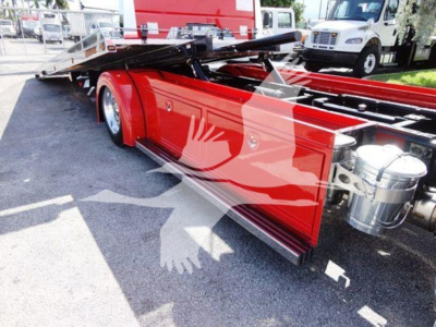 Peterbilt 337 rollback chassis with red side panels and hydraulic tow bed, visible storage tanks, and chrome exhaust components.