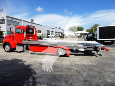 Peterbilt 337 rollback tow truck in red with a long silver and red tow carrier extending from the chassis, side view showing cab and flatbed equipment.