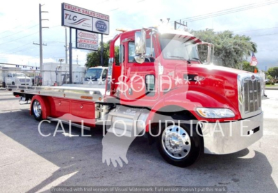 Peterbilt rollback truck shown in red with chrome front, long flatbed. Visible text: watermark 'SOLD' across image. Background includes TLC sign and utility poles.