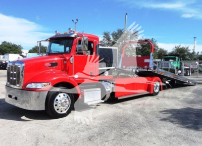 Peterbilt 337 rollback tow truck in red with a flatbed and hydraulic wheel lift visible; cab and chrome bumper; daytime outdoor lot.