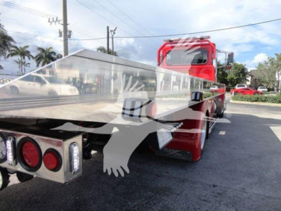 Peterbilt 337 rollback tow truck rear and flatbed section visible with red cab and chrome flatbed; license area shows lights and bumper; parking lot background.