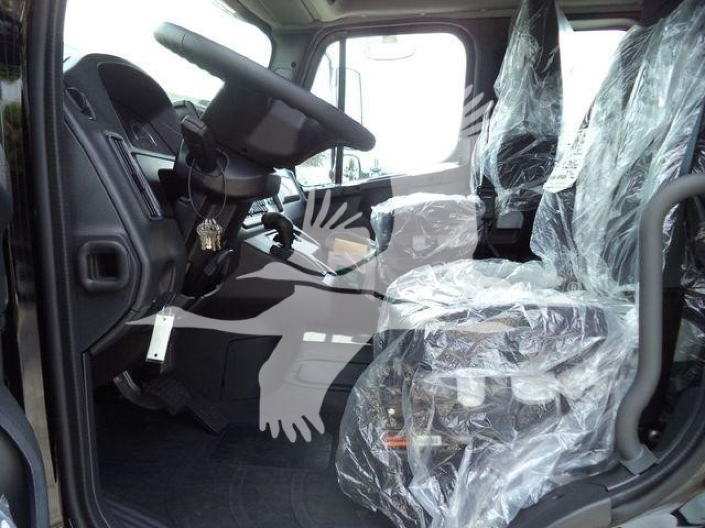 Dashboard and driver seat area of a new Freightliner M2 106 cab interior with plastic seat covers and steering wheel visible.
