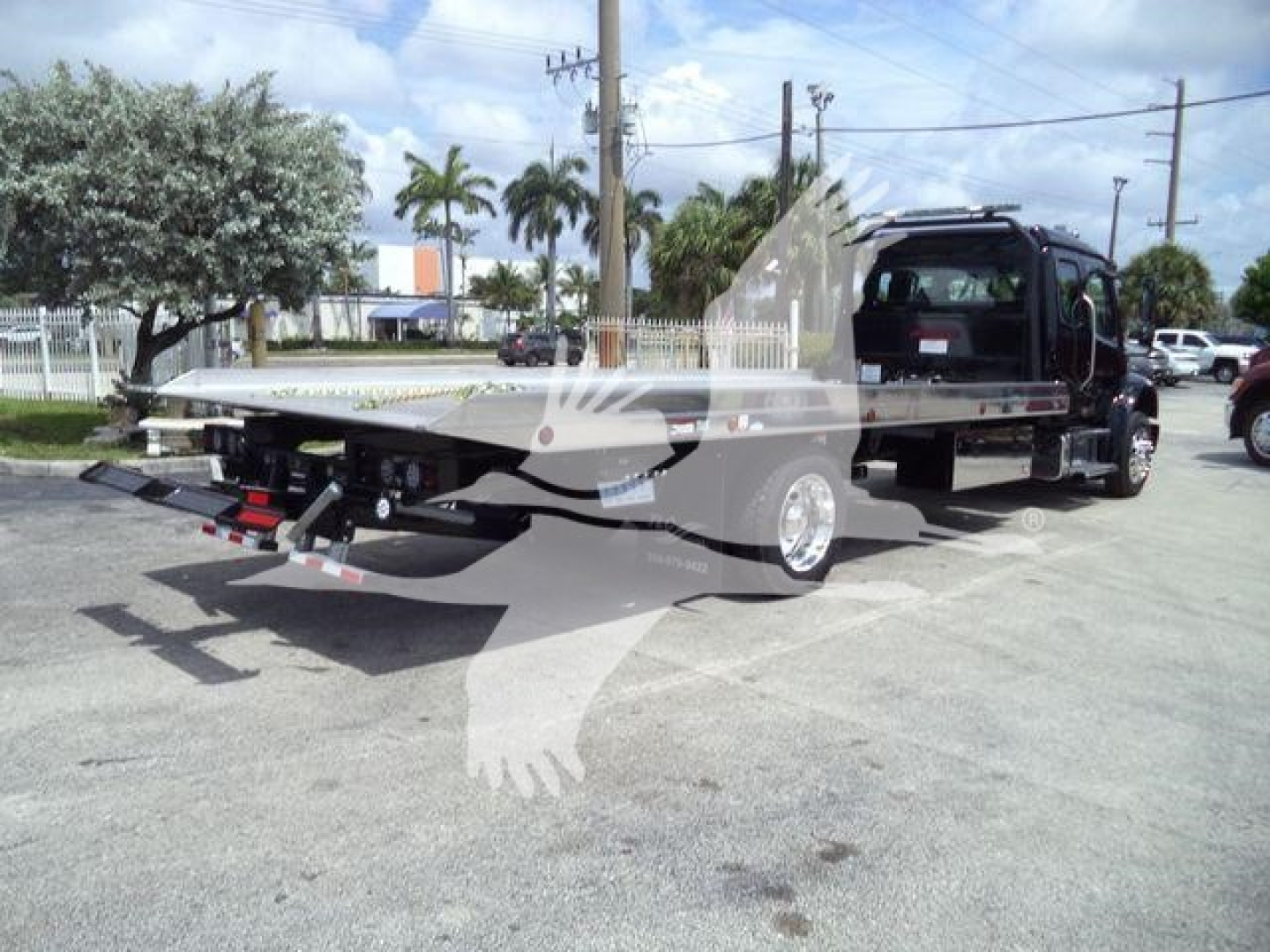 Flatbed rollback tow truck with hydraulic ramp and control area visible; no legible labels or fluid reservoirs readable on the photo.