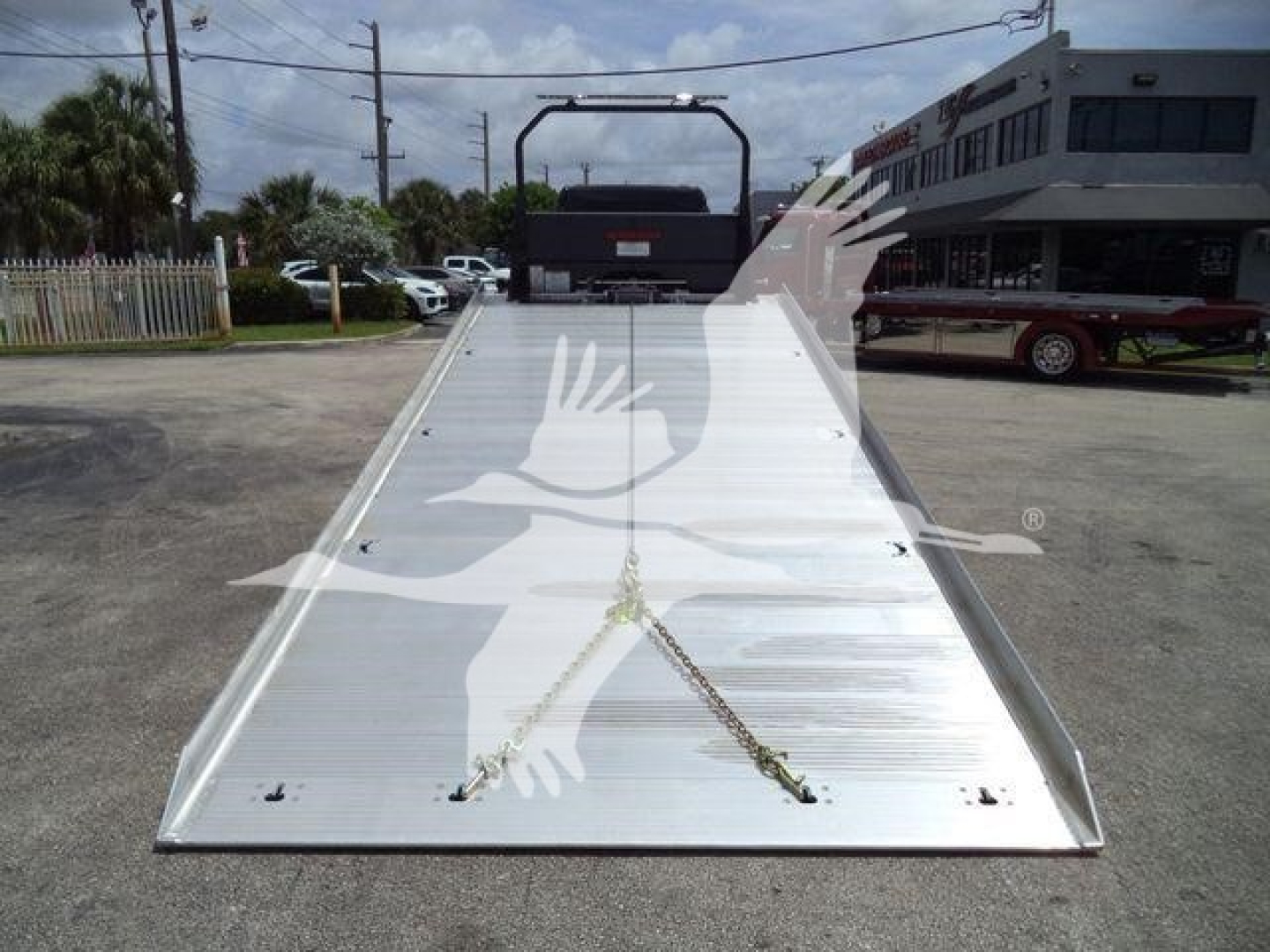 Freightliner M2 106 rollback bed showing aluminum incline with chains, rear hydraulic winch, and a rooftop truck in background.
