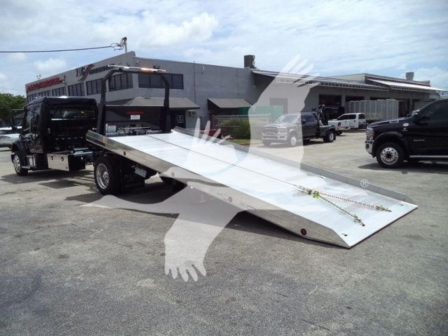 Freightliner M2 106 rollback truck with a long aluminum tilt bed and wheel-lift hardware in a dealership lot.