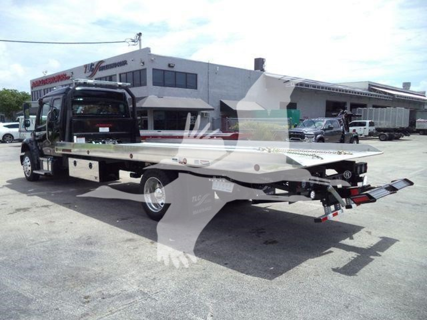 Truck bed rollback platform attached to a Freightliner M2 106 cab in a dealership lot showing tow truck flatbed and rear ramps.