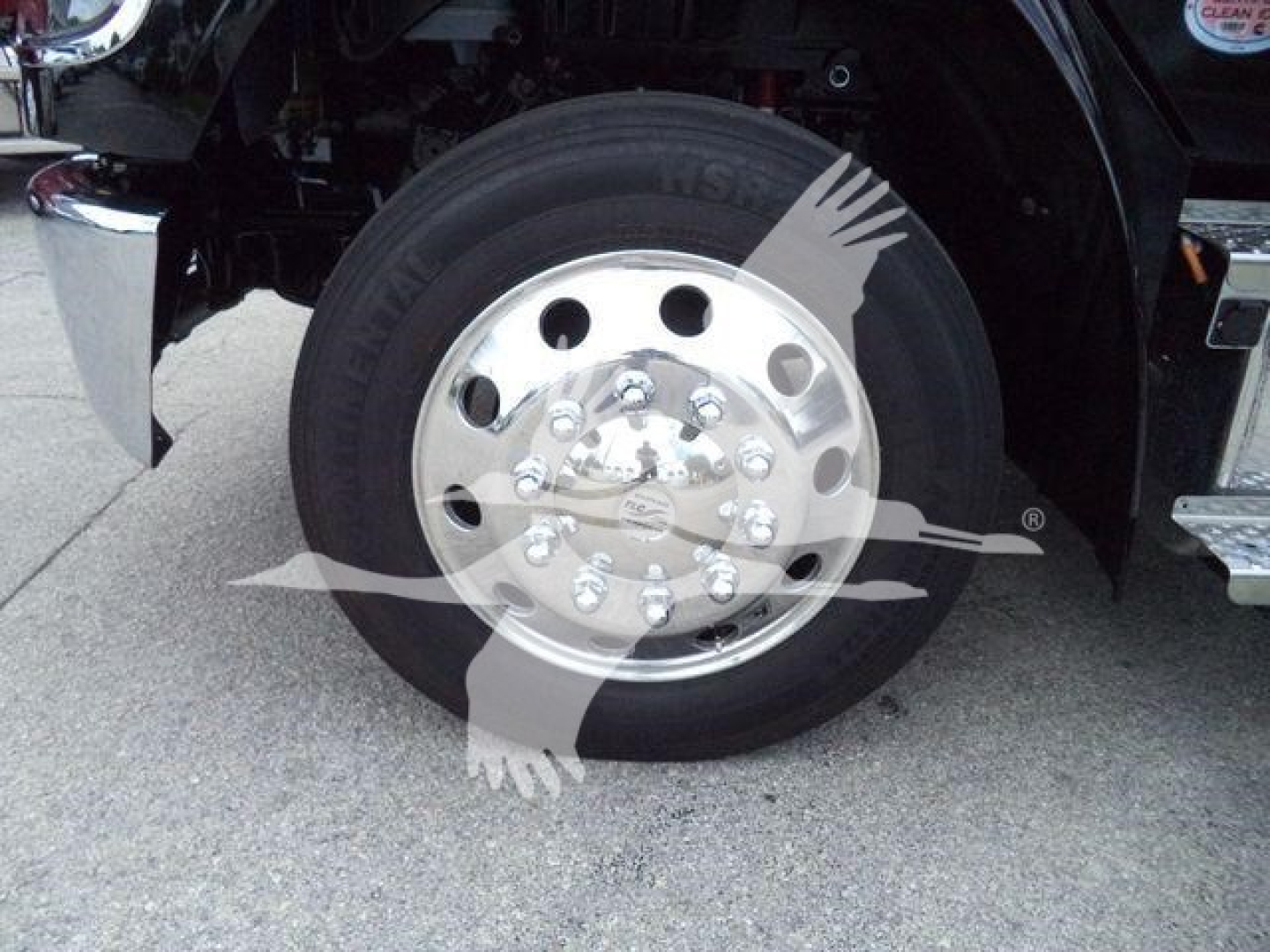 Wheel and tire close-up on a Freightliner M2 106 front suspension with chrome hub and lug nuts visible.