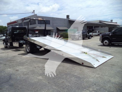 Freightliner M2 106 rollback truck with a long aluminum tilt bed and wheel-lift hardware in a dealership lot.