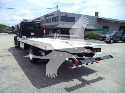 Freightliner M2 106 rollback truck bed with flatbed and hydraulic tow equipment, rear view showing platform and under-carriage, dealership backdrop
