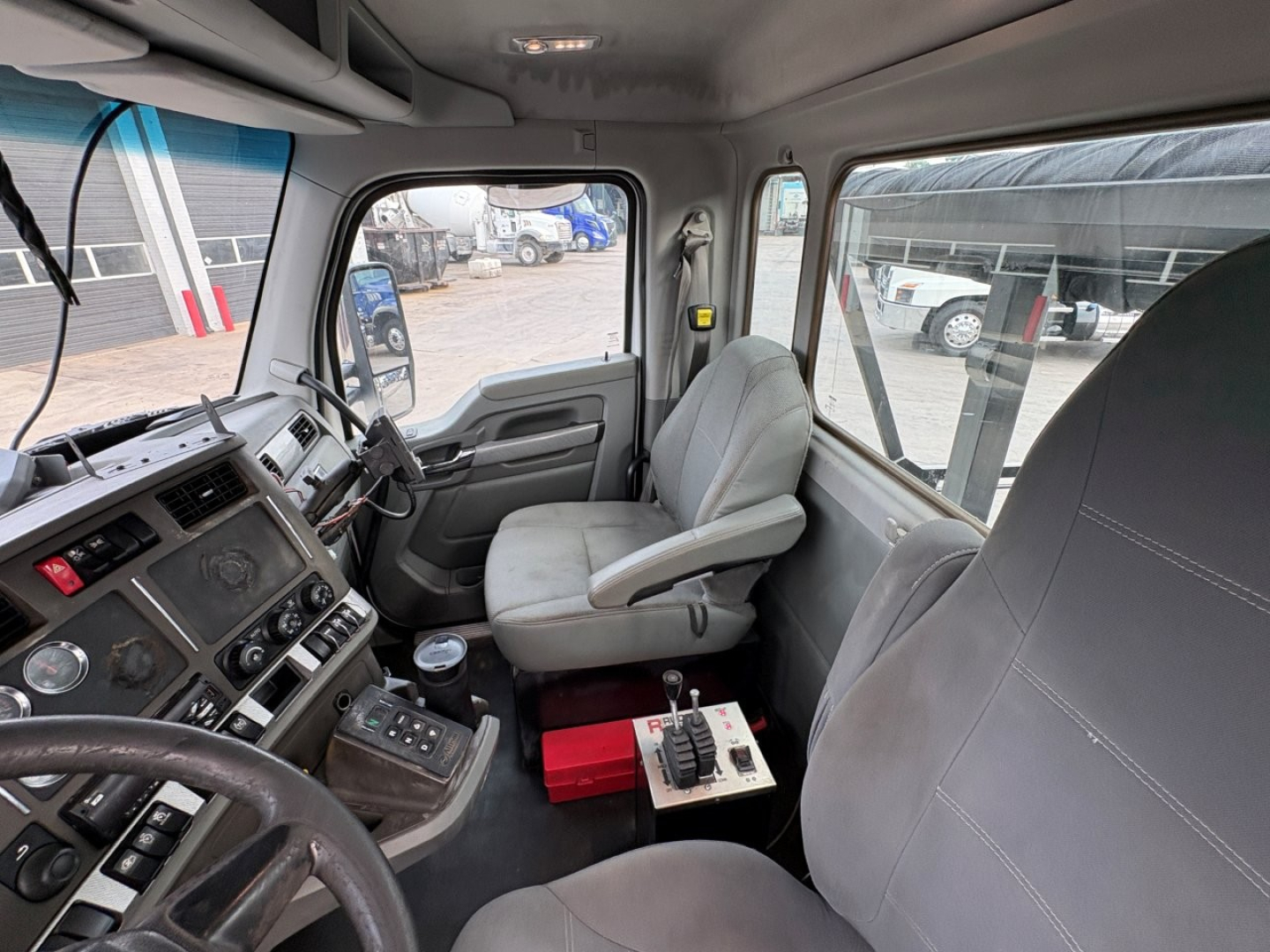 Truck cabin interior of a 2018 Kenworth T880 with gray seats and dashboard, showing steering wheel, control panels, gear shifter, and window views.
