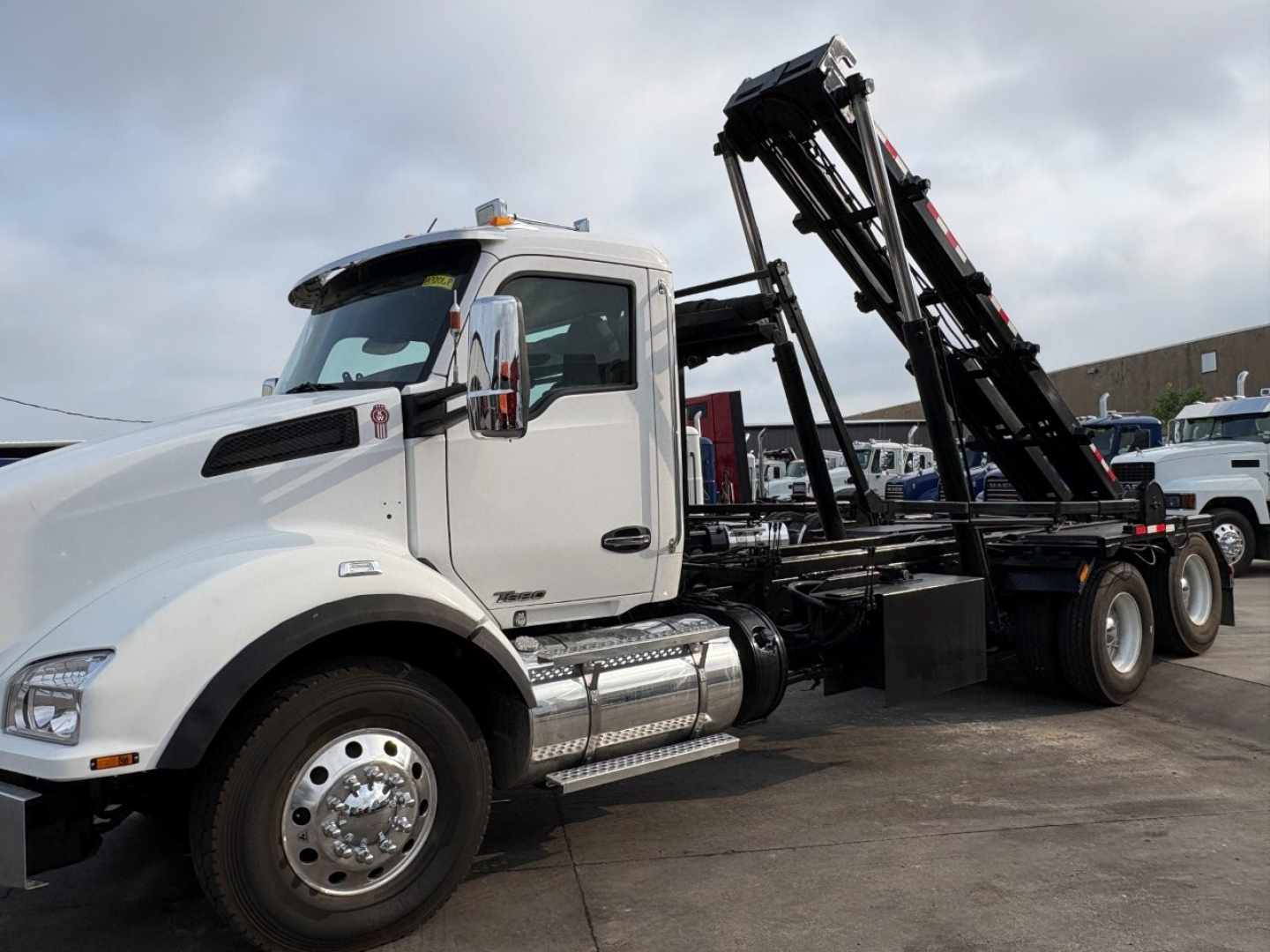 Kenworth T880 roll-off truck in white cab showing loading crane and hydraulic arms.