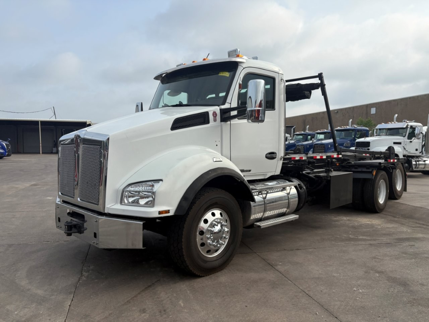 Truck image showing a white Kenworth T880 roll-off tractor with a large chrome grille, dual fuel tanks, and a flatbed rear for container hauling.