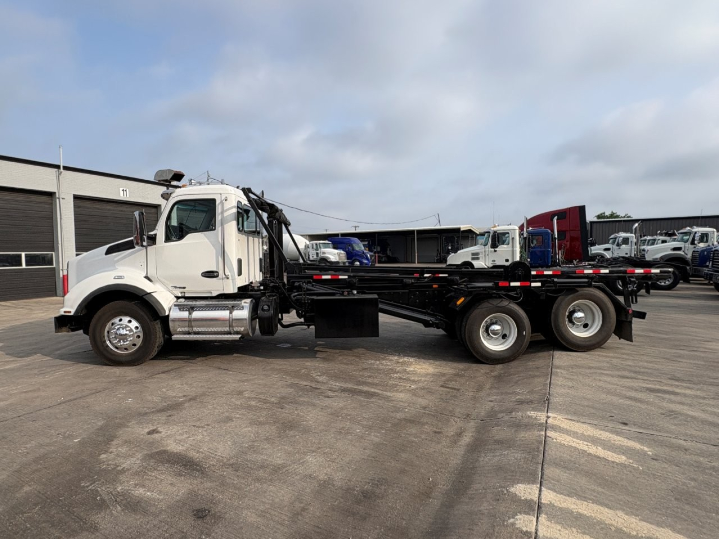 Kenworth T880 roll-off truck side view showing chassis and cab with long flatbed and three-axle rear suspension.