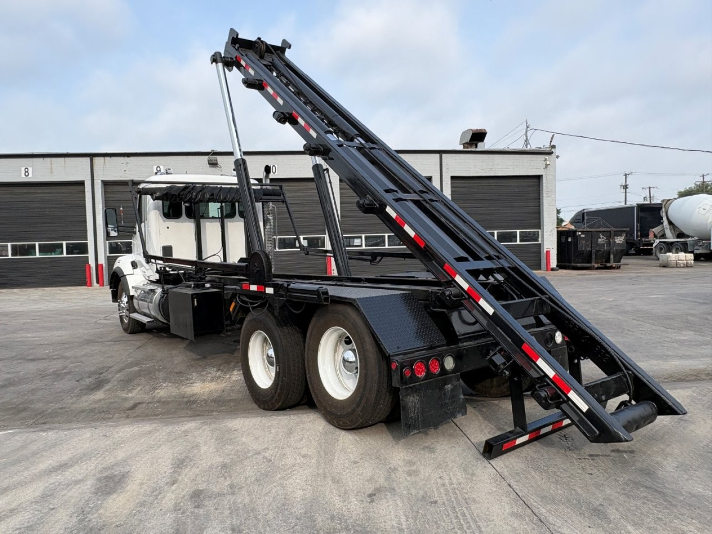 Kenworth T880 roll-off truck showing rear loading ramps and hydraulic hardware with twin rear axles and black framed bed.