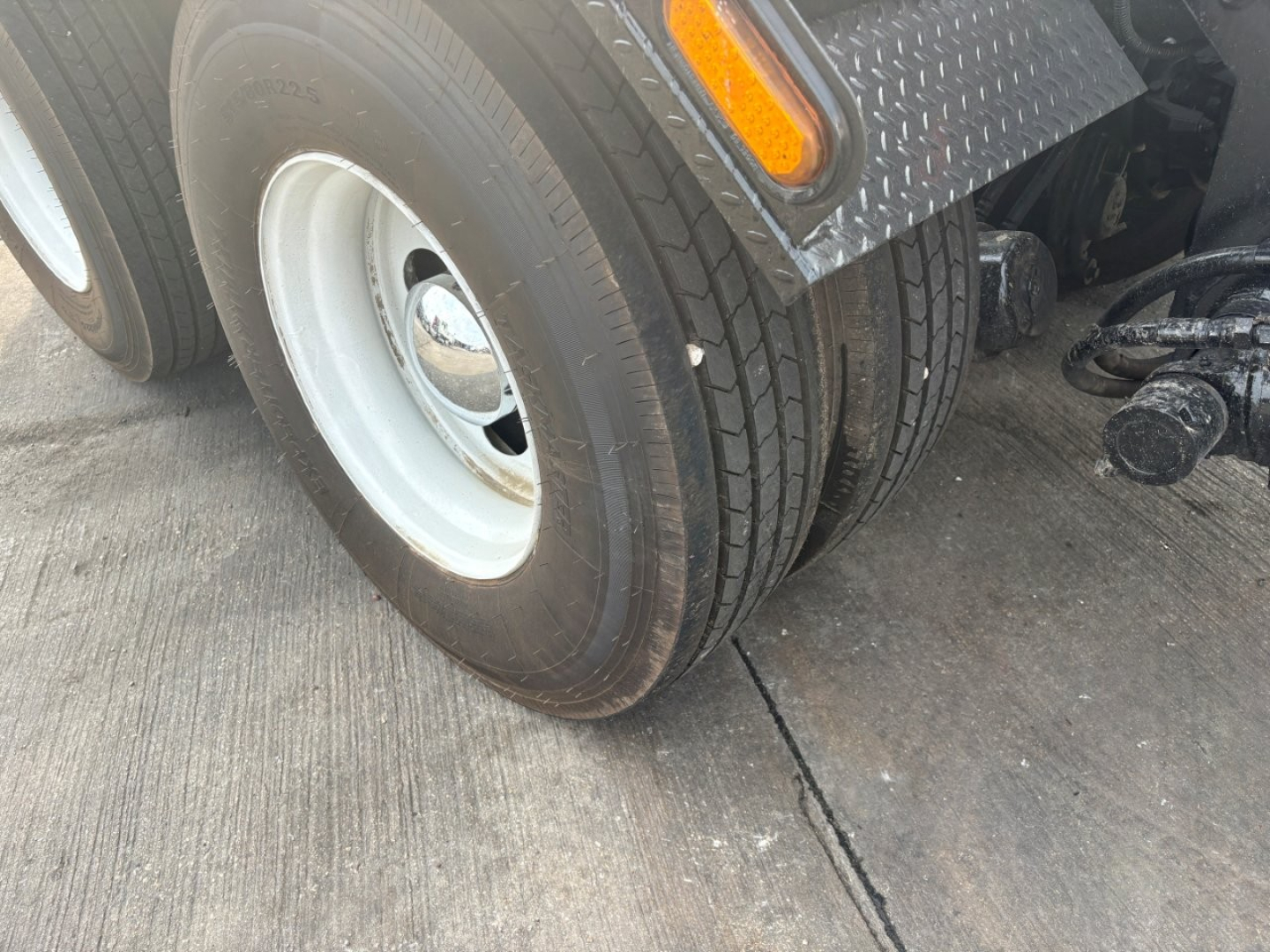 Kenworth T880 wheel and fender area showing dual rear wheels, tire tread, aluminum diamond plate step, and front of trailer hitch assembly.