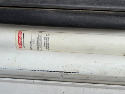 Kenworth label on a cylindrical rod showing model and serial information. Visible text includes KENWORTH and P-POWER? with a red vertical Kenworth logo.