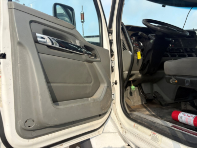 Kenworth T880 cab interior and open door showing steering wheel and dashboard with floor mat; doorway with light gray panel and chrome trim.