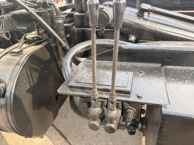 Kenworth T880 engine bay with gear levers and hydraulic control valves; visible labels show hoses and fittings, with metal tag on platform.