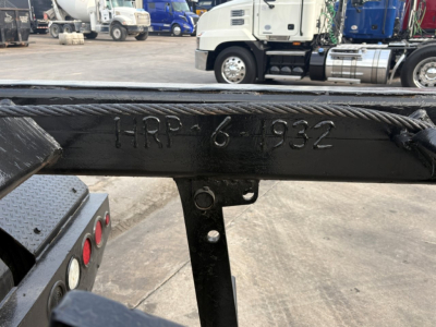 Frame rail with stamped numbers HRP-6 1932 and rope wound along top, trucks and equipment in background.