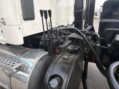 Kenworth T880 cab area with hydraulic control levers and engine bay view showing multiple levers and hoses near chrome fuel tank cover.