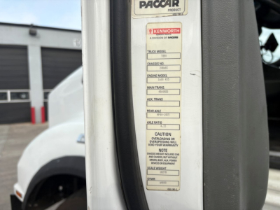 Truck body label showing Kenworth/Paccar badge and model/engine/transmission details on a vertical placard inside the door frame.