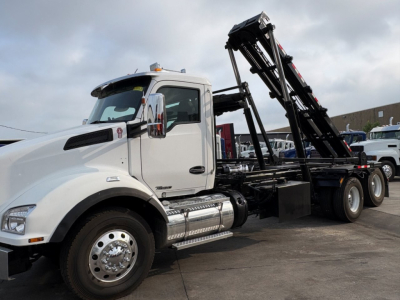 Kenworth T880 roll-off truck in white cab showing loading crane and hydraulic arms.