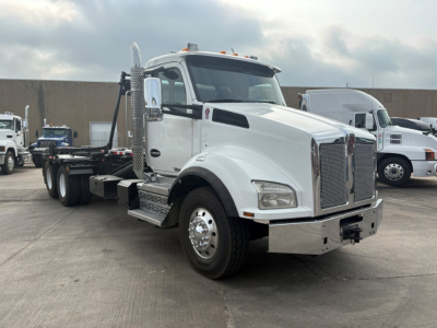 Kenworth T880 rolloff truck in white, front three-quarter view with chrome grille, large side mirrors, and flatbed chassis.