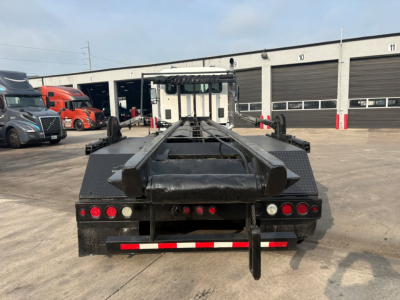 Kenworth T880 roll-off truck chassis rear view showing flatbed platform and taillights with red reflectors and warning bars.