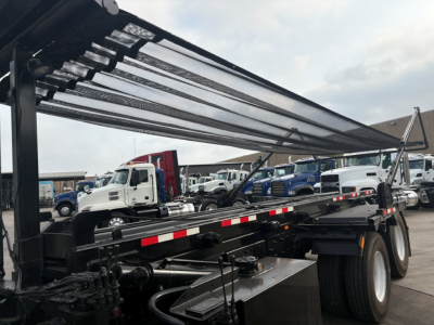 Kenworth T880 rolloﬀ tow truck chassis with hydraulic bed and tarp retracted, dual rear axles, cab in background, VIN tag area not visible.