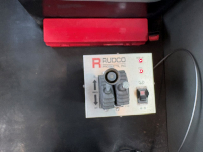 Kenworth T880 truck bed view showing RUDCO control panel with levers and buttons, part of roll-off system. Text 'RUDCO' and arrows on panel.