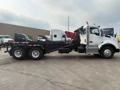 Kenworth T880 tow truck side view showcasing chassis and hydraulic rollback bed with black color, white cab, and metal steps.