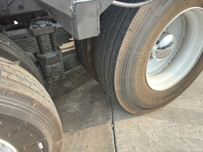 Kenworth T880 wheel and suspension area with dual rear axles, showing tire tread and hubcap, part of roll-off truck undercarriage.