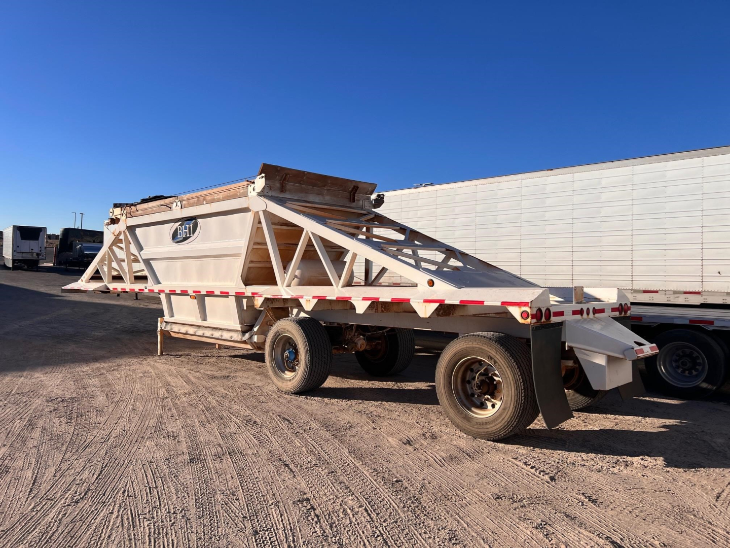 Manac light weight bottom dump trailer in side view showing chassis, dual rear wheels, and folded side panels.