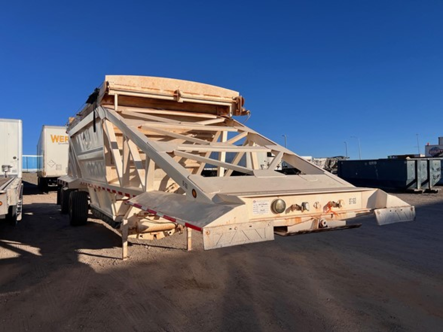 Manac light-weight bottom dump trailer in-yard showing rear and side framework, white with signage and latching mechanism.