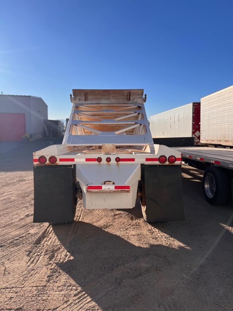 Manac light weight bottom dump trailer rear view showing mud flaps, taillights, and folded dumping bed in white with red reflective tape.