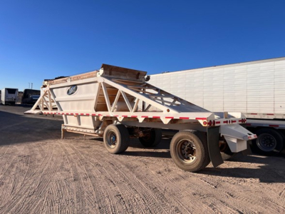 Bottom dump trailer showing Manac lightweight trailer with triangular frame and elevated bed, side warning decals visible.