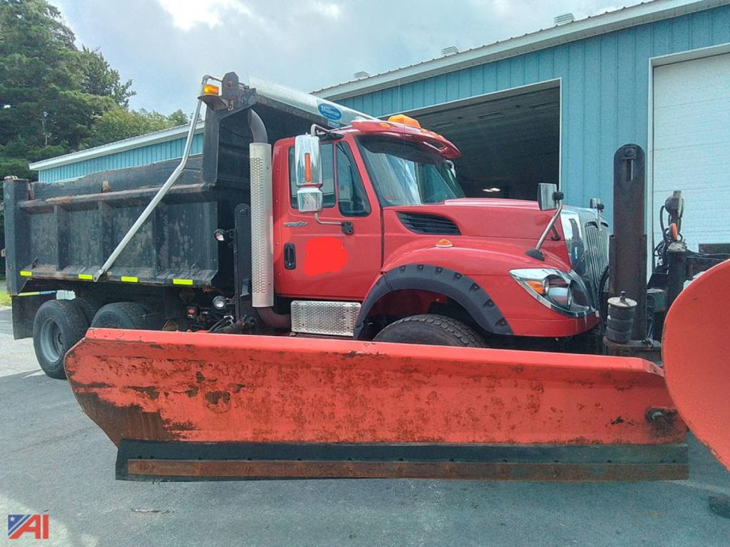 Dump truck cab and chassis with plow blade attached, red International WorkStar 7600, dump bed visible, front view at a service lot.