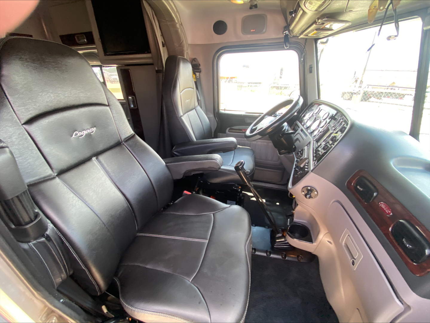 Peterbilt 389 interior view showing driver and passenger seats, dashboard, steering wheel, and gear lever.