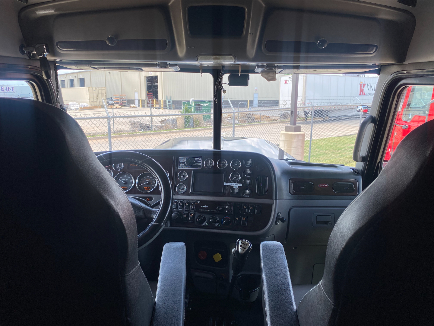 Peterbilt 389 cab interior view showing steering wheel, dashboard, and center console, with gear shifter and instrument gauges visible.