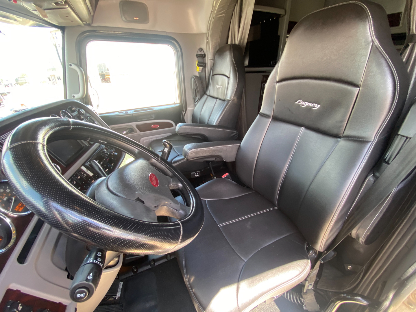 Peterbilt truck interior showing driver seat and steering wheel, black leather seats with stitched 'Peterbilt' emblem, dashboard and window view.