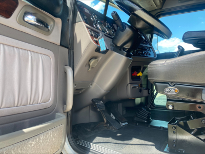Truck cab interior of a 2019 Peterbilt 389 showing driver's seat, dashboard, pedals, and door panel.