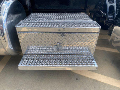 Conventional sleeper truck step box with diamond plate toolbox under the cab of a 2019 Peterbilt 389, chrome steps and black undercarriage visible.