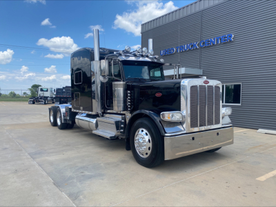 Peterbilt 389 conventional sleeper truck in front of a building, chrome bumper and exhaust stacks visible.