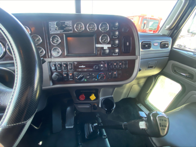 Peterbilt 389 cab interior showing dashboard gauges, steering wheel, shifter, and control switches.