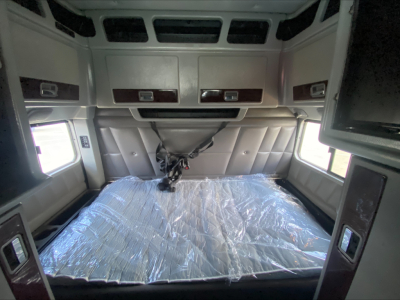 Peterbilt 389 truck sleeper cab interior with bed in plastic wrap, overhead cabinets, and side windows.