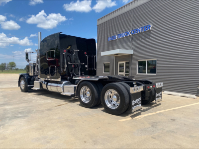 Peterbilt 389 tractor with black paint and chrome wheels, rear view showing dual rear axles and fifth wheel, parked outside a truck center.